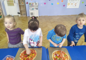 Dzieci ukladają na cieście poszczególne składniki pizzy.
